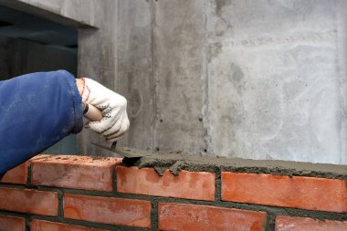 Hand with a trowel, in the process of laying a wall of red brick clipart