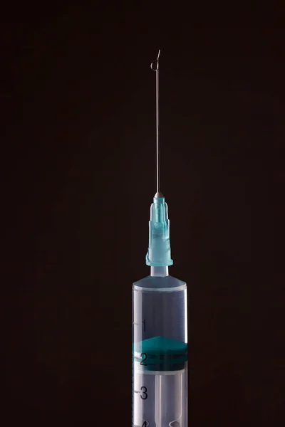 The end of the syringe with a needle filled with liquid on a dar — Stock Photo, Image