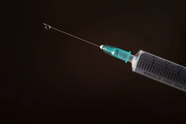 The end of the syringe with a needle filled with liquid on a dar — Stock Photo, Image
