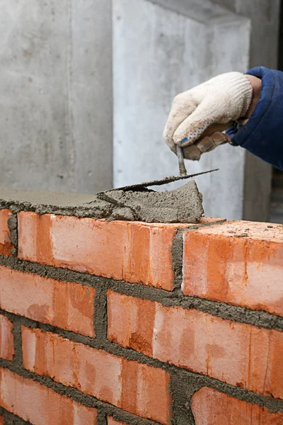 Mano con una paleta, en el proceso de colocación de una pared de ladrillo rojo —  Fotos de Stock