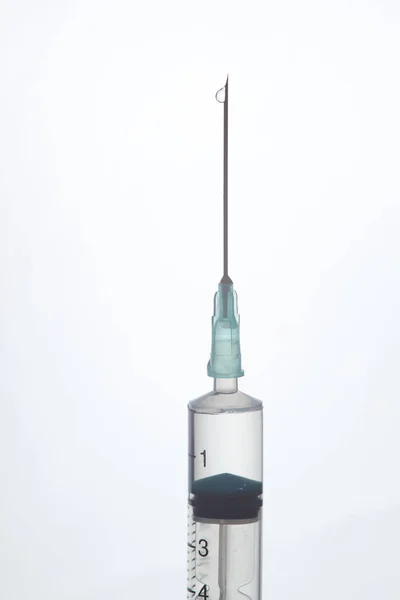 The end of the syringe with a needle filled with liquid on a lig — Stock Photo, Image