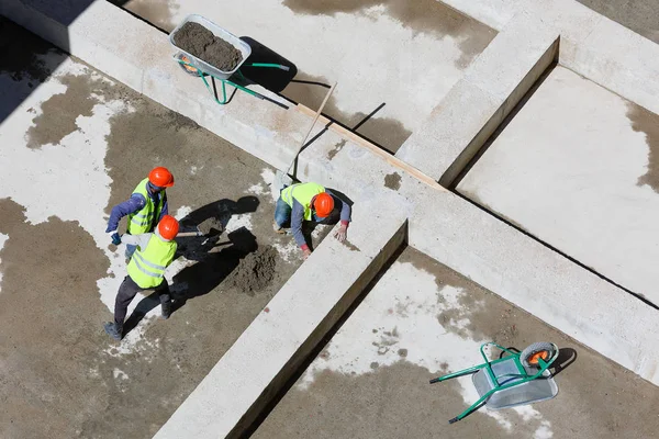 Uniformed workers clean sand on a construction site, top view.