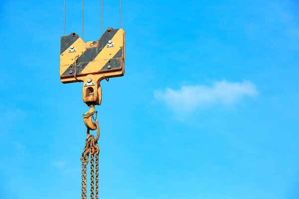 Crane load hook against the sky with trails and chain.