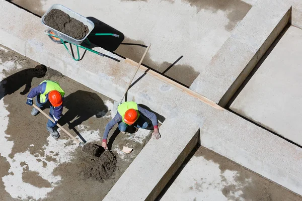 Uniformed workers clean sand on a construction site, top view.