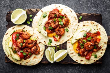 Düz fajitas ekmeği Kızarmış karides, biber ve soğan üzerinde ahşap kesme tahtası, üstten görünüm, avokado ve yeşil soğan ile servis içinde yatıyordu