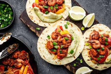 Düz fajitas ekmeği Kızarmış karides, biber ve soğan üzerinde ahşap kesme tahtası, üstten görünüm, avokado ve yeşil soğan ile servis içinde yatıyordu