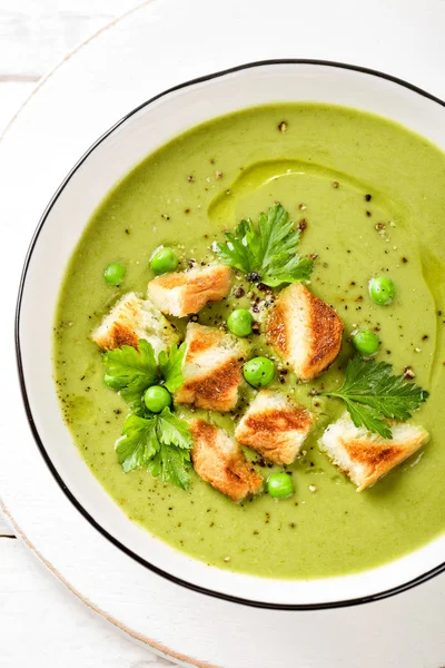 Pea soup. Green pea puree soup in a bowl served with grilled toasts, top view