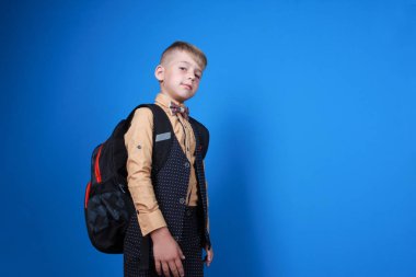 Üniforma, sırt çantası ve papyon giyen akıllı mutlu öğrenci. Mavi arka planda izole edilmiş çocuk. Okula, eğitime, reklam konseptine dönüş