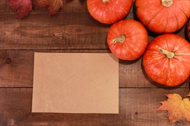 Turuncu balkabakları, kuru akçaağaç yaprakları, koyu kahverengi ahşap masadaki mesaj için boş kağıt. Hoşgeldiniz sonbahar, hasat festivali, Cadılar Bayramı, Şükran Günü konsepti. Üst görünüm, alanı kopyala