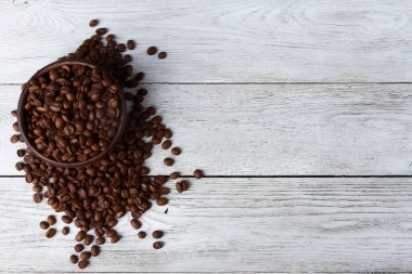 Beyaz ahşap arka planda kil kasede kahve çekirdekleri. Yakın çekim, kopyalama alanı, üst görünüm. Arap tohumları, rosto, kafein konsepti