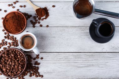 Taze espresso bardakları, metal Türk tenceresi, kil kaselerde kızartılmış Arap fasulyeleri, öğütülmüş kahve tozu, tahta masada kaşık. Üst görünüm, boşluğu kopyala. Kahve dükkanı, sabah, baristaların işyeri konsepti.
