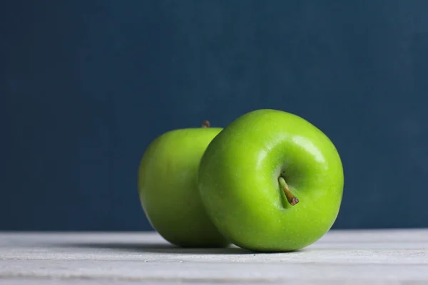 Fresh green apples on white table surface with dark blue wall in background. Close-up. School snacks or organic food concept
