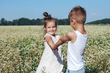Mutlu aktif erkek ve kız el ele tutuşup çiçek çayırlarında dans ediyorlar. Çocuklar açık havada eğleniyor. Yaz, tatil, çocukluk kavramı