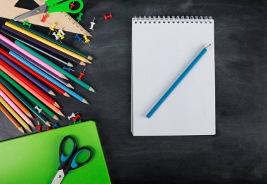 Defterin boş sayfası. Renkli kalemler, yeşil defter, makas, raptiyeler, tahta zemin üzerinde cetvel. Üst görünüm, kopyalama alanı, düz yatış. Okul malzemeleri ya da ofis kırtasiyesi konsepti