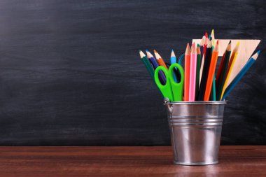 Renkli kalemler, makas ve cetvel kahverengi ahşap masa üzerinde, arka planda karatahta desenli. Yakın çekim, kopyalama alanı. Okul konseptine dönelim.