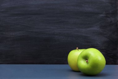 Arka planda karatahta desenli koyu mavi masada iki taze yeşil elma. Yatay kopyalama uzayı, yakın plan. Okul atıştırmalıkları veya organik gıda konsepti