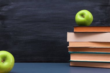 Koyu mavi masadaki yeşil elmalar ve yığınla kitap karatahta ve arka plandaki tebeşir çizgilerine karşı. Yan görüş, kopyalama alanı, yakın çekim. Öğrenme, eğitim, bilgi, kütüphane, aşk okuma kavramı