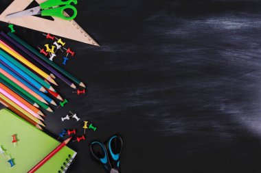 Renkli kalemler, yeşil defter, makas, rapa, tahta üzerinde çizgili cetvel. Üst manzara, düz yatak, arka plan. Okul malzemeleri ya da ofis kırtasiyesi konsepti