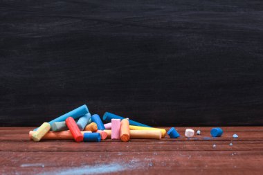 Kahverengi ahşap masadaki tebeşir kırıntıları ve kara tahta parçaları. Yan görüş, kopyalama alanı, yakın çekim. Okula dönüyorum, çizim konsepti.