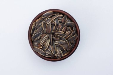 Beyaz arka planda izole edilmiş ayçiçeği tohumlarıyla dolu bir kase. Üst manzara, yakın çekim, daire şeklinde. Gıda, hasat, tarım, tarım kavramı