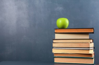 Masadaki kitap yığınının üzerinde koyu mavi duvar arka planına karşı yeşil elma. Yan görüş, kopyalama alanı, yakın çekim, izole nesneler. Öğrenme, eğitim, bilgi, kütüphane, aşk okuma kavramı