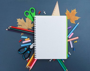 Mavi kalemli beyaz defter sayfası, metin için kopyalama alanı. Fotokopi kitabı, makas, cetvel, kalemler, koyu mavi arka planda sonbahar yaprakları. Üst manzara, düz yatış. Sonbahar konseptiyle okula dönüyorum.