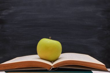 Tahta zemine karşı açık bir kitap sayfasında yeşil elma. Yan görüş, kopyalama alanı, yakın çekim. Öğrenme, eğitim, bilgi, kütüphane, aşk okuma kavramı