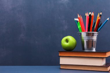 Koyu mavi duvar arka planına karşı istiflenmiş kitapların üzerinde yeşil elma ve kalem saksısı. Yan görüş, kopyalama alanı, yakın çekim. Öğrenim, eğitim, okul malzemeleri konsepti