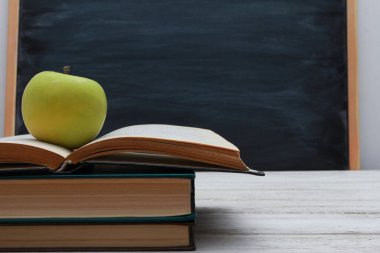 Yeşil elma ve okul tahtasındaki beyaz tahta masadaki istiflenmiş kitaplar üzerine açık ders kitabı. Yan görüş, yakın çekim, kopyalama alanı. Öğrenme, eğitim, bilgi, kütüphane, aşk okuma kavramı