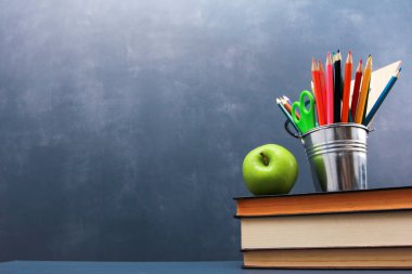 Taze elma ve bir yığın kitabın üzerinde koyu mavi duvar arka planına karşı bir kazan kalem. Yan görüş, kopyalama alanı, yakın çekim, alçak açı. Öğrenim, eğitim, okul malzemeleri konsepti
