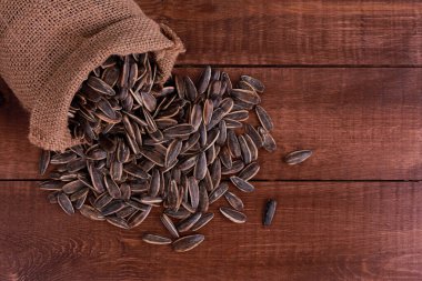 Çuvalla ayçiçeği çekirdeği kahverengi ahşap masaya saçılmış. Üst görünüm, boşluğu kopyala. Gıda, hasat, tarım, tarım kavramı