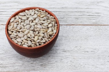 Beyaz ahşap masanın üzerinde bir kase ayçiçeği çekirdeği. Yüksek açı, yakın çekim, kopyalama alanı. Gıda, hasat, tarım, tarım kavramı