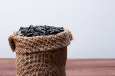 Kahverengi ahşap masada siyah ayçiçeği tohumlarıyla dolu bir çanta. Yan görüş, yakın çekim, kopyalama alanı. Gıda, hasat, tarım, tarım kavramı