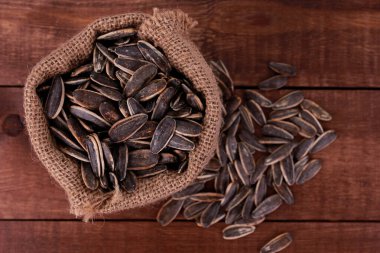 Kahverengi ahşap masadaki çuval bezinde ayçiçeği tohumları yığını. Üst görünüm, yakın çekim, kopyalama alanı. Gıda, hasat, tarım, tarım kavramı