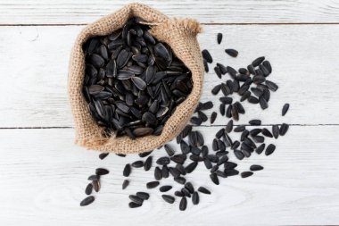 Beyaz ahşap masaya saçılmış siyah ayçiçeği tohumları yığını. Üst manzara, yakın çekim. Gıda, hasat, tarım, tarım kavramı