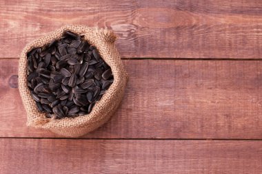 Kahverengi ahşap masada bir çuval siyah ayçiçeği çekirdeği. Üst görünüm, yakın çekim, kopyalama alanı. Gıda, hasat, tarım, tarım kavramı