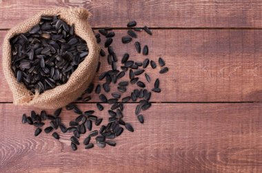 Kahverengi ahşap masada çuvaldaki siyah ayçiçeği tohumları yığını. Üst görünüm, yakın çekim, kopyalama alanı. Gıda, hasat, tarım, tarım kavramı