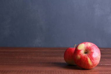 Kahverengi ahşap masada, arka planda koyu mavi duvar ve fotokopi alanı olan iki olgun kırmızı elma. Doğal organik gıda, sağlıklı beslenme, hasat mevsimi konsepti