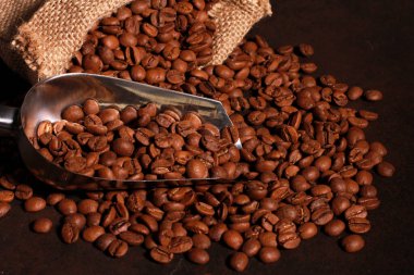 Çuval bezinden siyah masaya saçılmış metal kepçeli kahve çekirdekleri. Yakın planda kızartılmış Arap taneleri. Kahve dükkanı, kafein, rosto konsepti.