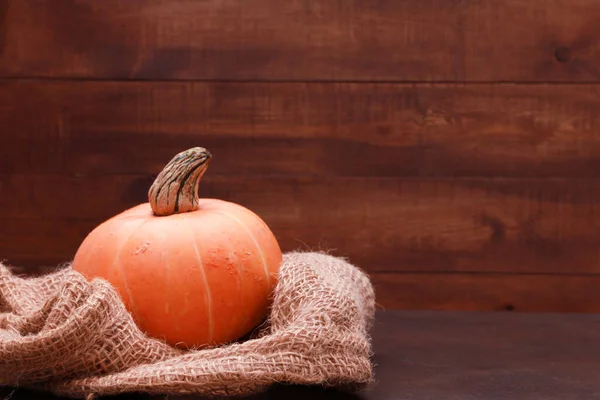 Orange pumpkin, burlap sack against dark brown wooden wall background. Side view, copy space, closeup. Food, autumn, holiday, thanksgiving, harvest season concept.