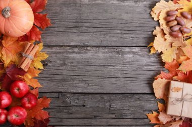 Turuncu balkabağı, baharat, elma, meşe palamudu, el işi hediye kutusu, kaba ahşap tahtaların üzerine renkli yapraklar. Boşluğu, çerçeveyi, sınırı kopyala. Sonbahar, hasat, Şükran Günü konsepti