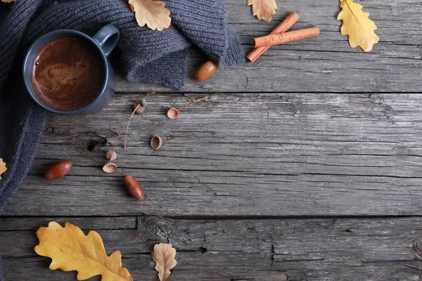 Black coffee mug, oak leaves, acorns, grey scarf, cinnamon on rough old wooden boards. Copy space, top view. Autumn background, fall season, thanksgiving, coffee shop menu concept