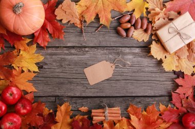 Turuncu balkabağı, baharat, elma, meşe palamudu, el işi hediye kutusu ve etiket, grunge ahşap arka planda renkli yapraklar. Boşluğu, çerçeveyi, sınırı kopyala. Sonbahar, satış, hasat, şükran günü konsepti