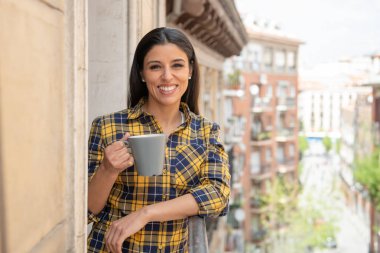 Sabah kahve. Güleryüzlü ve sıcak kahve ilk fincan gün evde açık balkon keyfi içme mutlu güzel latin bir kadın. Kentsel arka plan. Ev konfor yaşam tarzı
