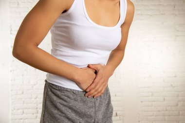 Genç bir kadının karnı üzerinde el ele tutuşarak acı karın ağrısı olan kapatın. Vücut ağrı, gastrit, kabızlık, adet ağrısı ve adet krampları. Sağlık kavramı