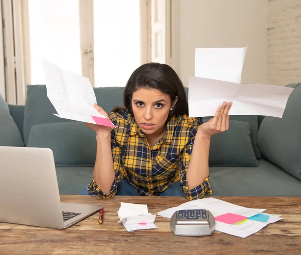 Young worried woman in stress banking and accounting debt bills, bank papers, expenses and payments with computer at home feeling desperate in a bad financial situation.