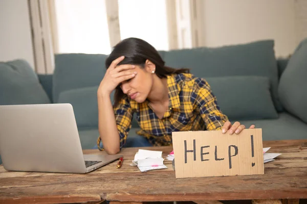 Young worried woman in stress banking and accounting debt bills, bank papers, expenses and payments with computer at home asking for help feeling desperate in a bad financial situation.