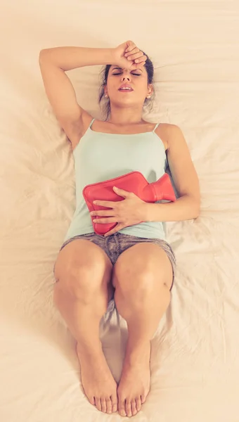 若いラテン系美人胃けいれんと悲しいベッドで横になっている腹に対してホット水のボトルを保持している月経痛に苦しんでいる痛みを伴う式で 女性女性医療の概念 — ストック写真
