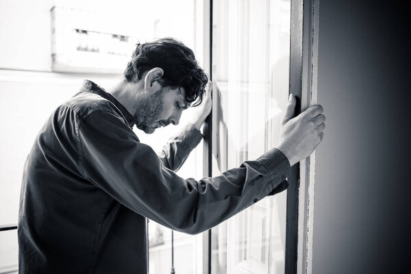 Lonely young man looking outside house balcony looking depressed, destroyed, sad and suffering emotional crisis and grief thinking of taking a difficult and important life decision