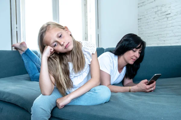 Digital technology addicted mum using her smart phone ignoring her sad Little girl feeling abandoned and unhappy with her mum not paying attention to her. Phone addiction and parenting behavior.